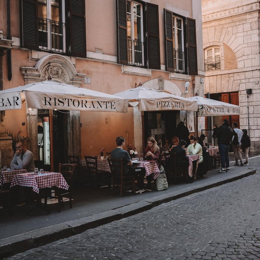 people sitting by tables on sidewalk by restaurant